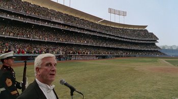 Movie still from “The Naked Gun: From the Files of Police Squad!” (1988), directed by David Zucker – An older man is speaking at a baseball game; Extreme Wide shot, High angle