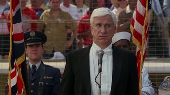 Movie still from “The Naked Gun: From the Files of Police Squad!” (1988), directed by David Zucker – A man in a suit and tie standing in front of a crowd; Medium shot, Low angle