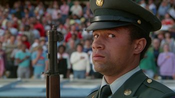 Movie still from “The Naked Gun: From the Files of Police Squad!” (1988), directed by David Zucker – A man in uniform holding a rifle in front of a crowd of onlookers; Close Up shot, Low angle