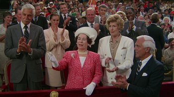 Movie still from “The Naked Gun: From the Files of Police Squad!” (1988), directed by David Zucker – A group of people standing in front of an audience; Medium shot, Low angle