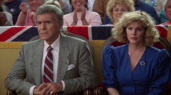 Movie still from “The Naked Gun: From the Files of Police Squad!” (1988), directed by David Zucker – A man and a woman sitting next to each other in front of a crowd; Medium shot, Low angle