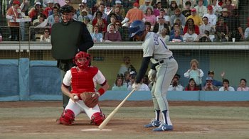Movie still from “The Naked Gun: From the Files of Police Squad!” (1988), directed by David Zucker – A baseball player swinging a bat on a field; Wide shot, Over the shoulder angle