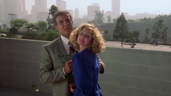 Movie still from “The Naked Gun: From the Files of Police Squad!” (1988), directed by David Zucker – A man and a woman posing for a picture in front of a wall; Medium shot, Low angle