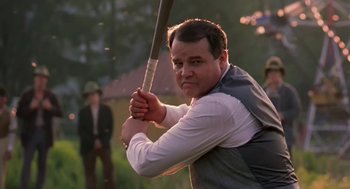 Movie still from “The Natural” (1984), directed by Barry Levinson – A man holding a baseball bat while standing next to a tree; Medium shot, Over the shoulder angle