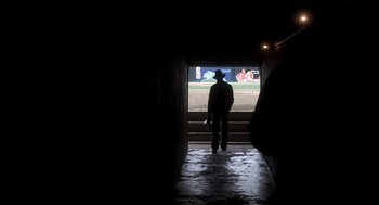 Movie still from “The Natural” (1984), directed by Barry Levinson – A man standing in a dark room looking out a window; Wide shot, Low angle