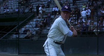 Movie still from “The Natural” (1984), directed by Barry Levinson – A baseball player is holding a baseball bat in front of a crowd of people; Medium shot, Low angle