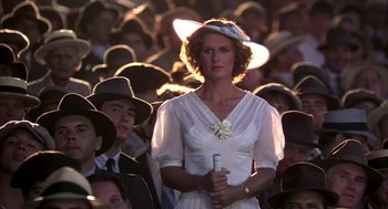 Movie still from “The Natural” (1984), directed by Barry Levinson – A woman in a white dress holding a pen in front of a group of people; Medium shot, Low angle