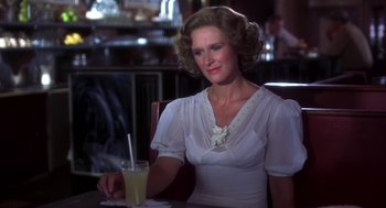 Movie still from “The Natural” (1984), directed by Barry Levinson – A woman sitting at a table holding a drink; Close Up shot, Over the shoulder angle