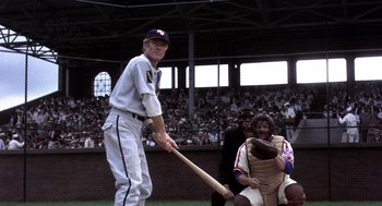 Movie still from “The Natural” (1984), directed by Barry Levinson – A baseball player holding a baseball bat on top of a baseball field; Medium shot, Over the shoulder angle