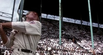 Movie still from “The Natural” (1984), directed by Barry Levinson – A baseball player swinging a bat in front of an audience; Medium shot, Low angle