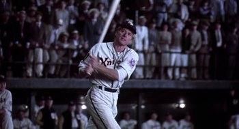 Movie still from “The Natural” (1984), directed by Barry Levinson – A man swinging a baseball bat in front of a crowd of people; Medium shot, Low angle