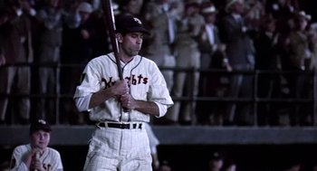 Movie still from “The Natural” (1984), directed by Barry Levinson – A man holding a baseball bat while standing on a baseball field; Medium shot, Low angle