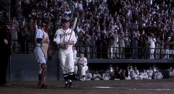 Movie still from “The Natural” (1984), directed by Barry Levinson – A man holding a baseball bat on top of a baseball field; Wide shot, Over the shoulder angle