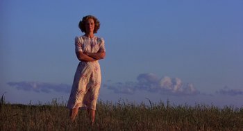 Movie still from “The Natural” (1984), directed by Barry Levinson – A woman standing in a field with her arms crossed; Wide shot, Low angle