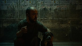 Movie still from “Charlie Countryman” (2013), directed by Fredrik Bond – A man sitting next to a brown and black dog; Medium shot, Low angle