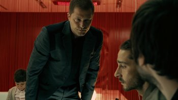 Movie still from “Charlie Countryman” (2013), directed by Fredrik Bond – A man standing in front of another man in front of a red wall; Medium shot, Over the shoulder angle