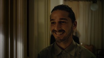 Movie still from “Charlie Countryman” (2013), directed by Fredrik Bond – A man smiling for the camera while standing next to a wall; Close Up shot, Over the shoulder angle