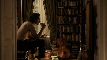 Movie still from “Charlie Countryman” (2013), directed by Fredrik Bond – A man sitting on a chair in front of a violin; Medium shot, Over the shoulder angle