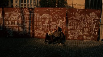 Movie still from “Charlie Countryman” (2013), directed by Fredrik Bond – Two people sitting in front of a wall with graffiti on it; Wide shot, Overhead angle