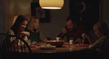 Movie still from “The Nest” (2020), directed by Sean Durkin – A group of people sitting around a dinner table; Medium shot, High angle