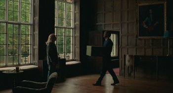 Movie still from “The Nest” (2020), directed by Sean Durkin – A man and woman walking in front of a large window; Wide shot, Low angle