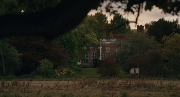 Movie still from “The Nest” (2020), directed by Sean Durkin – An old brick building with a large tree in front of it; Extreme Wide shot, High angle