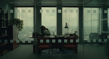 Movie still from “The Nest” (2020), directed by Sean Durkin – A man sitting at a desk in front of a large window; Extreme Wide shot, High angle