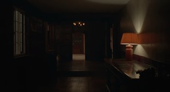 Movie still from “The Nest” (2020), directed by Sean Durkin – A dark room with a table and lamp in it; Extreme Wide shot, High angle