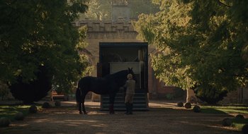 Movie still from “The Nest” (2020), directed by Sean Durkin – A man standing next to a horse in a field; Wide shot, Low angle