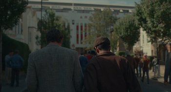 Movie still from “The Nest” (2020), directed by Sean Durkin – Two men walking down the street in front of a building; Wide shot, Over the shoulder angle