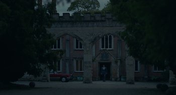 Movie still from “The Nest” (2020), directed by Sean Durkin – A man standing in front of an old brick building; Extreme Wide shot, Low angle