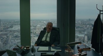 Movie still from “The Nest” (2020), directed by Sean Durkin – An older man sitting at a desk in an office overlooking a city; Medium shot, Over the shoulder angle