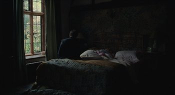 Movie still from “The Nest” (2020), directed by Sean Durkin – A person sitting on a bed in a dark room; Wide shot, High angle