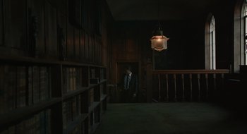 Movie still from “The Nest” (2020), directed by Sean Durkin – A man standing in a dark room next to a book shelf; Wide shot, Over the shoulder angle