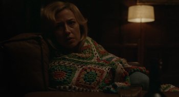 Movie still from “The Nest” (2020), directed by Sean Durkin – A woman sitting at a table covered in a crocheted blanket; Medium shot, Over the shoulder angle