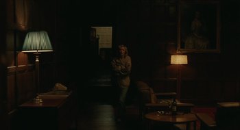 Movie still from “The Nest” (2020), directed by Sean Durkin – A person standing in a dark room holding something in their hands; Wide shot, High angle