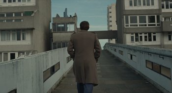 Movie still from “The Nest” (2020), directed by Sean Durkin – A man wearing a coat walking down a bridge; Wide shot, Low angle