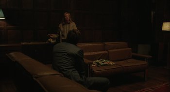 Movie still from “The Nest” (2020), directed by Sean Durkin – Two people sitting on couches in a dark room; Medium shot, Over the shoulder angle