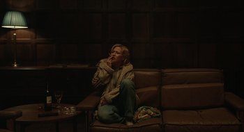 Movie still from “The Nest” (2020), directed by Sean Durkin – A woman sitting on a couch smoking a cigarette; Medium shot, High angle