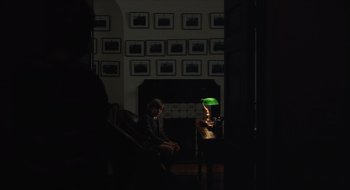 Movie still from “The Nest” (2020), directed by Sean Durkin – A person sitting in a chair in front of a lamp; Wide shot, Over the shoulder angle