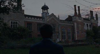 Movie still from “The Nest” (2020), directed by Sean Durkin – A man standing in front of an old brick building; Extreme Wide shot, Low angle