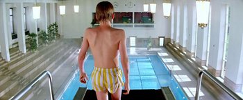 Movie still from “The NeverEnding Story II: The Next Chapter” (1990), directed by George Miller – A young boy in a swim suit standing in front of an indoor pool; Wide shot, Low angle