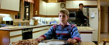 Movie still from “The NeverEnding Story II: The Next Chapter” (1990), directed by George Miller – A boy sitting at a table in a kitchen; Medium shot, Over the shoulder angle