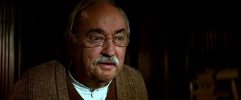 Movie still from “The NeverEnding Story II: The Next Chapter” (1990), directed by George Miller – An older man wearing glasses and a sweater; Close Up shot, Low angle