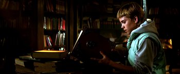 Movie still from “The NeverEnding Story II: The Next Chapter” (1990), directed by George Miller – A young boy looking at an open book in a dark room; Close Up shot, Low angle