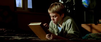 Movie still from “The NeverEnding Story II: The Next Chapter” (1990), directed by George Miller – A boy is reading a book on the floor; Close Up shot, Low angle