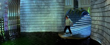 Movie still from “The NeverEnding Story II: The Next Chapter” (1990), directed by George Miller – A man standing on top of a platform near a body of water; Wide shot, High angle