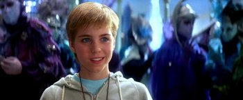 Movie still from “The NeverEnding Story II: The Next Chapter” (1990), directed by George Miller – A young boy is smiling for the camera in front of a crowd; Close Up shot, Over the shoulder angle