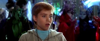 Movie still from “The NeverEnding Story II: The Next Chapter” (1990), directed by George Miller – A young boy with a blue shirt is looking at the camera; Close Up shot, Over the shoulder angle