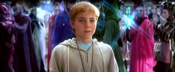 Movie still from “The NeverEnding Story II: The Next Chapter” (1990), directed by George Miller – A young boy in front of a group of people; Close Up shot, Over the shoulder angle